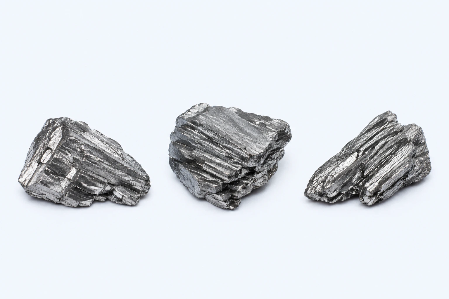 Three gray elemental arsenic fragments with layered brittle crystalline fracture faces.