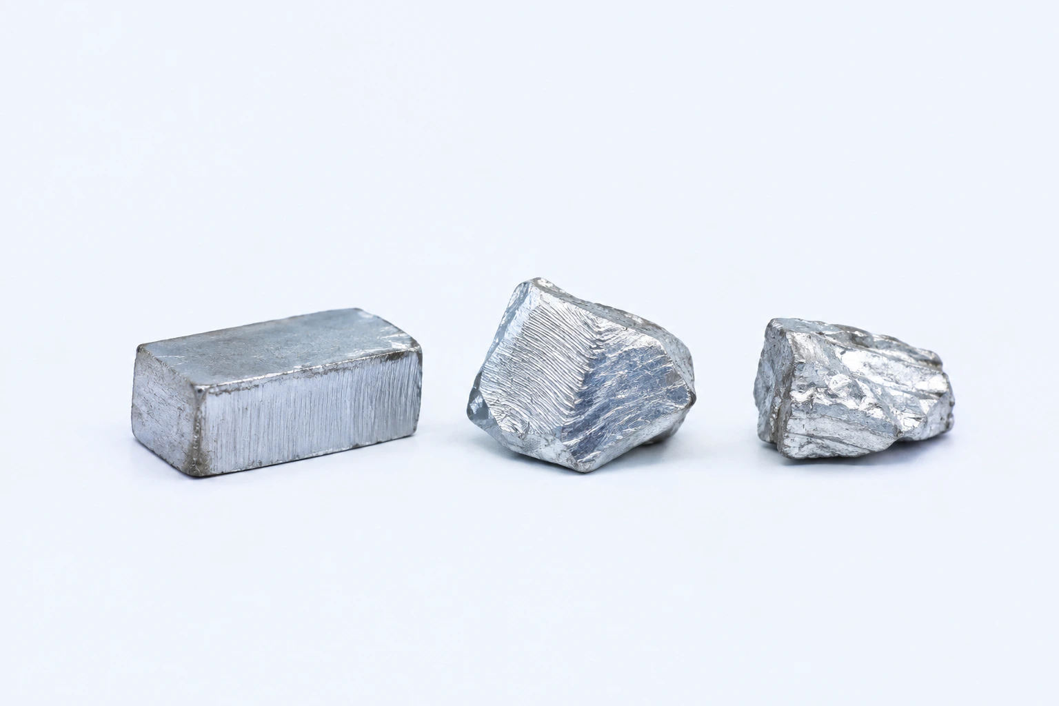 Three elemental cadmium specimens: one short low bar and two irregular blue-tinged silver-white pieces.
