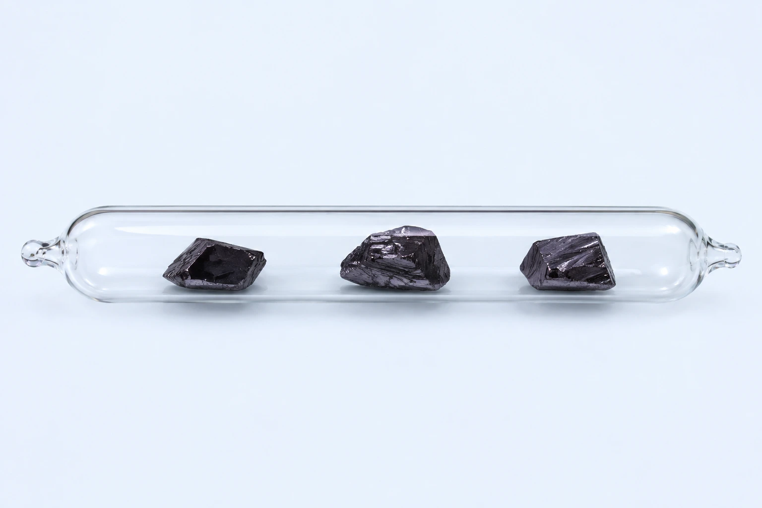 A sealed clear ampoule containing three separated dark gray-violet elemental iodine crystals.