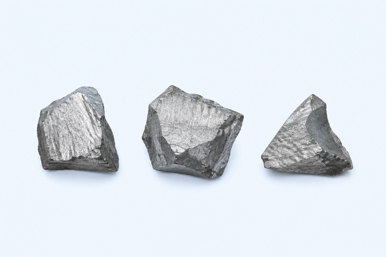 Three elemental manganese fragments with angular gray surfaces and broad metallic fracture faces.