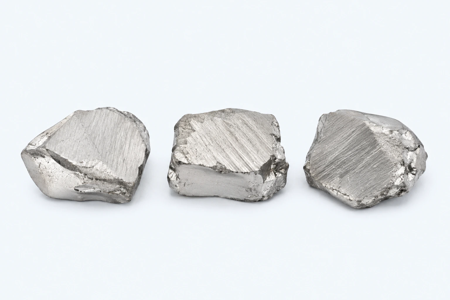 Three white-tin elemental specimens with soft-looking silvery-white worked surfaces.